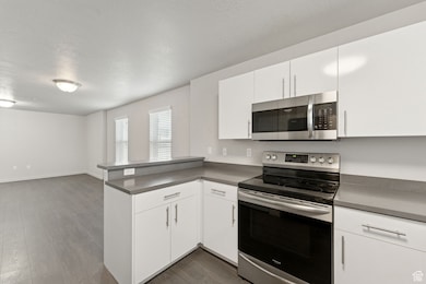 Kitchen with appliances with stainless steel finishes, dark countertops, white cabinetry, and a textured ceiling