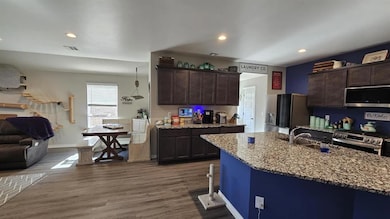 Kitchen with appliances with stainless steel finishes, dark brown cabinets, light stone counters, recessed lighting, and wood finished floors