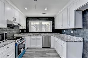 Kitchen with appliances with stainless steel finishes, under cabinet range hood, light stone countertops, and white cabinets