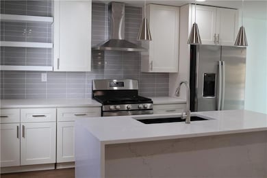 Kitchen featuring white cabinetry, wall chimney ra