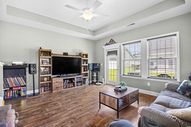 Living room featuring a raised ceiling, wood finished floors, and a ceiling fan