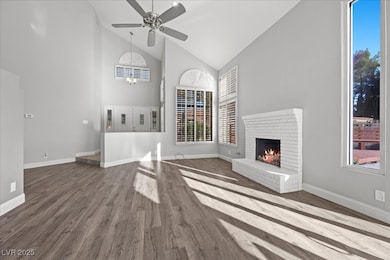 Unfurnished living room featuring high vaulted ceiling, dark wood-type flooring, a brick fireplace, and a ceiling fan