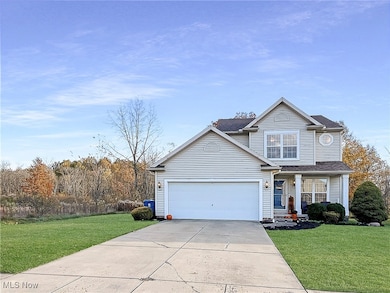 Traditional home featuring a front lawn, concrete driveway, a shingled roof, and a garage