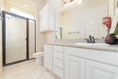 Bright bathroom with a large walk-in shower, featuring glass doors and neutral tile. It includes a spacious vanity with granite countertops, under-sink storage, and modern fixtures.