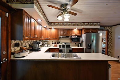 Kitchen featuring stainless steel appliances, under cabinet range hood, a sink, a peninsula, and light countertops