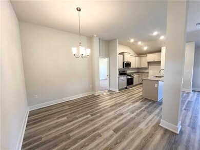 Kitchen with stainless steel appliances, a chandelier, lofted ceiling, dark wood-style floors, and decorative light fixtures