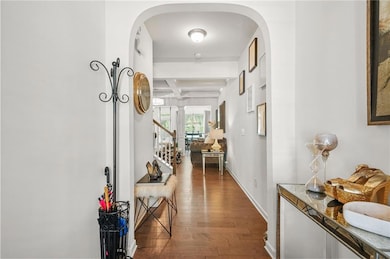 Hallway featuring dark wood-style flooring, beamed ceiling, coffered ceiling, arched walkways, and stairs