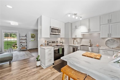 Kitchen with appliances with stainless steel finishes, stone countertops, tasteful backsplash, white cabinetry, upgraded dishwasher, and wood-style floors.