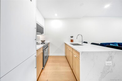 Kitchen featuring a peninsula, light wood-type flooring, stainless steel appliances, light stone counters, and white cabinets