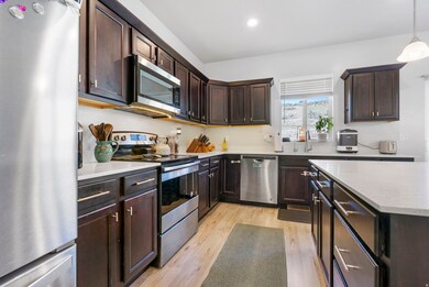 Kitchen featuring appliances with stainless steel finishes, dark brown cabinets, light wood finished floors, decorative light fixtures, and recessed lighting