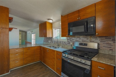 Kitchen featuring gas stove, black microwave, light stone counters, tasteful backsplash, and dark wood-type flooring