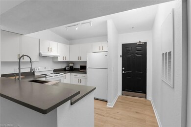Kitchen with white appliances, under cabinet range hood, dark countertops, rail lighting, and a peninsula