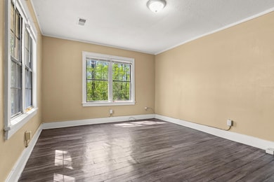 Empty room with a textured ceiling, baseboards, dark wood-style floors, and visible vents