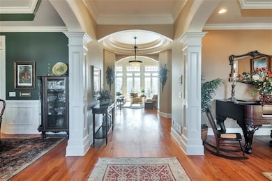 Foyer with crown molding, a decorative wall, decorative columns, and light wood-style floors