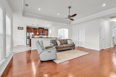 Living room featuring arched walkways, a tray ceiling, a ceiling fan, light wood finished floors, and baseboards
