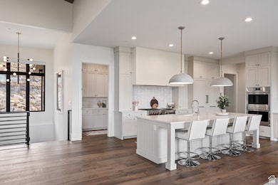 Kitchen featuring decorative light fixtures, a breakfast bar area, stainless steel double oven, a center island with sink, and backsplash