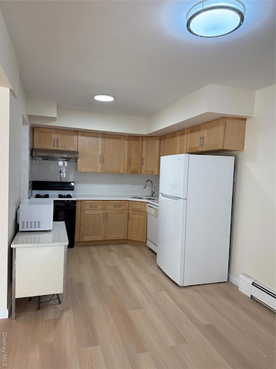 Kitchen featuring light countertops, refrigerator, range, a baseboard radiator, and light wood finished floors