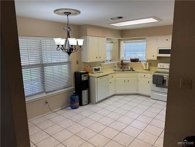 Kitchen with white appliances, a sink, light countertops, a chandelier, and light tile patterned floors
