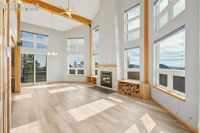 Unfurnished living room featuring beamed ceiling, a ceiling fan, light wood-style flooring, a fireplace with flush hearth, and a towering ceiling