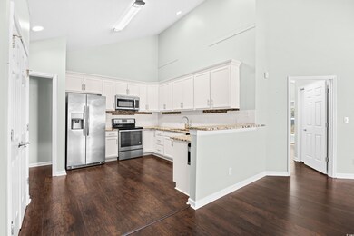 Kitchen featuring backsplash, white cabinetry, high vaulted ceiling, appliances with stainless steel finishes, and a peninsula