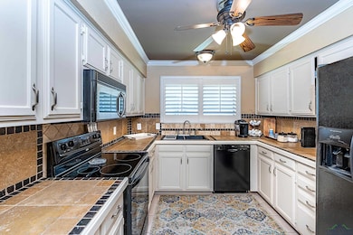 Kitchen featuring black appliances, ceiling fan, tile counters, crown molding, and backsplash