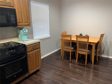 Kitchen with light countertops, black appliances, dark wood-style flooring, and brown cabinets