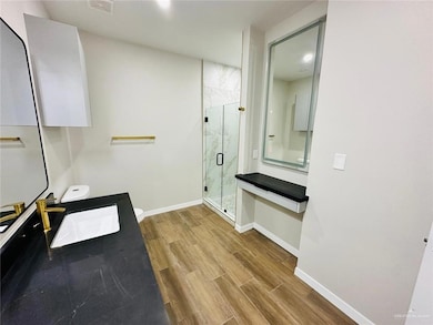 Full bathroom with a marble finish shower, wood finished floors, baseboards, and vanity