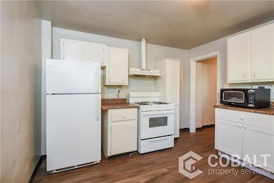 Kitchen with white appliances, under cabinet range hood, white cabinetry, and dark wood-style floors