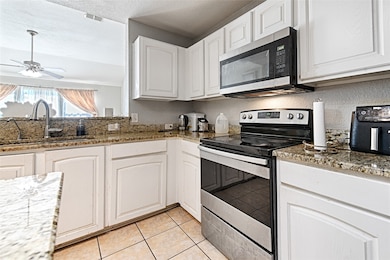 Kitchen with appliances with stainless steel finishes, white cabinets, light tile patterned floors, light stone countertops, and a ceiling fan