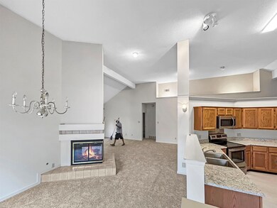 Kitchen featuring appliances with stainless steel finishes, open floor plan, light colored carpet, brown cabinetry, and a fireplace