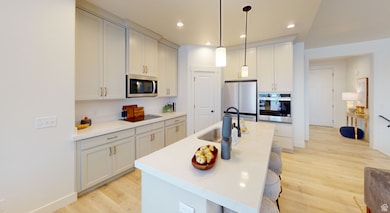 Kitchen featuring light wood-type flooring, stainless steel appliances, recessed lighting, a breakfast bar, and decorative light fixtures