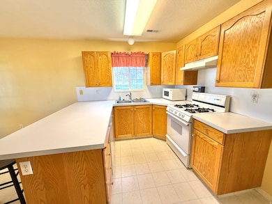 Kitchen featuring a peninsula, white appliances, light countertops, under cabinet range hood, and brown cabinetry