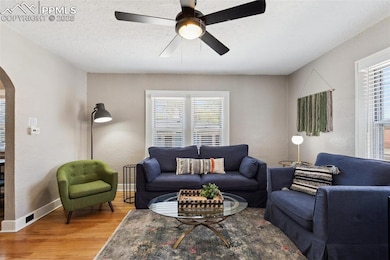 Living room featuring wood flooring, a wealth of natural light, a ceiling fan, and arched walkways.