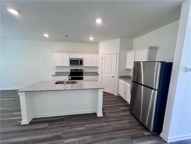 Kitchen with appliances with stainless steel finishes, a sink, dark wood-style floors, a center island with sink, and white cabinetry