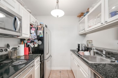Kitchen featuring appliances with stainless steel finishes, light tile patterned flooring, and white cabinetry