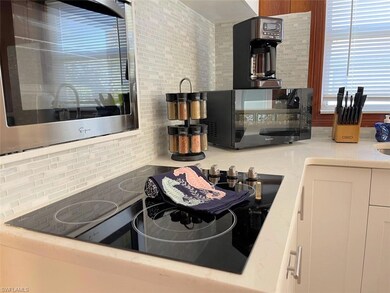 Kitchen featuring appliances, light stone counters, backsplash, and white cabinetry