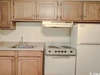 Kitchen featuring white appliances, under cabinet range hood, a sink, and light countertops