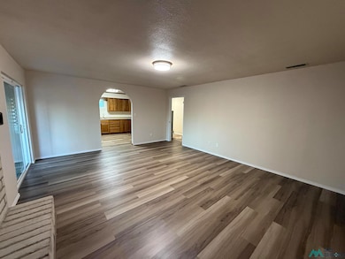 Unfurnished living room with arched walkways, light wood finished floors, and a textured ceiling