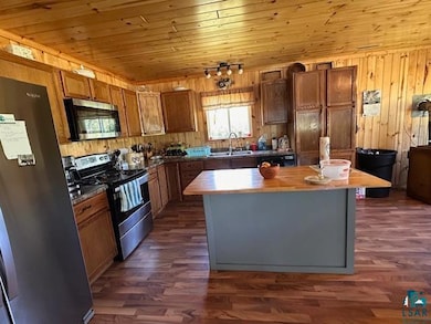 Kitchen with appliances with stainless steel finishes, a center island, wood walls, dark wood-style floors, and wood ceiling