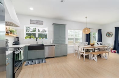 Kitchen with appliances with stainless steel finishes, light wood-type flooring, custom exhaust hood, hanging light fixtures, and open shelves