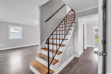 Stairway with wood finished floors, ornamental molding, plenty of natural light, and a textured ceiling