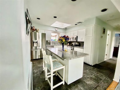 Kitchen featuring appliances with stainless steel finishes, a breakfast bar area, a kitchen island, white cabinetry, and backsplash