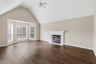 Unfurnished living room with a premium fireplace, a textured ceiling, dark wood-style floors, lofted ceiling, and ceiling fan