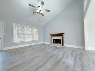 Unfurnished living room featuring high vaulted ceiling, a premium fireplace, light wood finished floors, and ceiling fan
