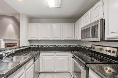 Kitchen featuring a brick fireplace, dark stone counters, stainless steel appliances, light tile patterned floors, and white cabinets