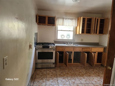 Kitchen featuring stainless steel gas range, a sink, open shelves, dark countertops, and glass insert cabinets