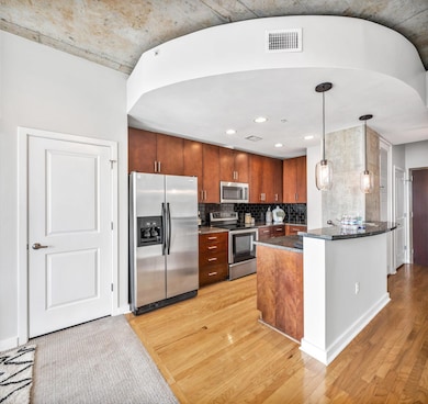 Kitchen featuring dark stone countertops, stainless steel appliances, decorative backsplash, pendant lighting, and light wood-style floors