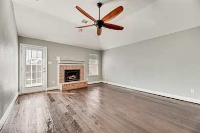 Unfurnished living room featuring lofted ceiling, a brick fireplace, wood finished floors, and a ceiling fan