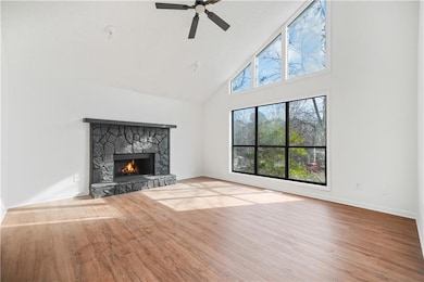 Unfurnished living room featuring high vaulted ceiling, wood finished floors, a stone fireplace, baseboards, and ceiling fan