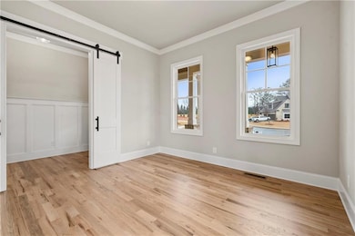 Unfurnished room with plenty of natural light, light wood-style flooring, a barn door, ornamental molding, and a decorative wall